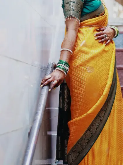 A detail shot of the bride's hands on the railing, showing off her mehndi and the beautiful texture of her yellow silk saree.