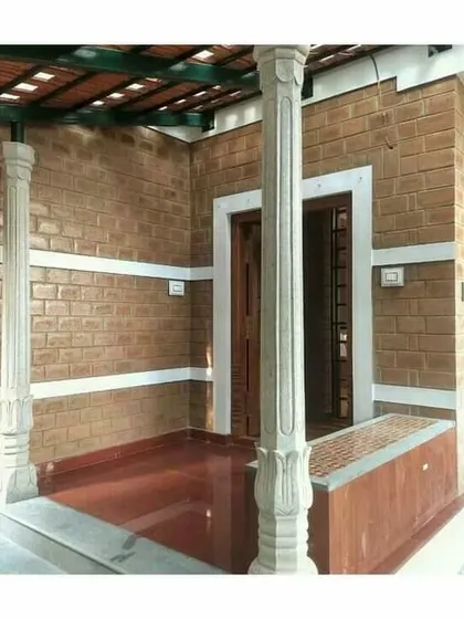 A verandah space with traditional stone pillars, exposed brick, and a red oxide floor.