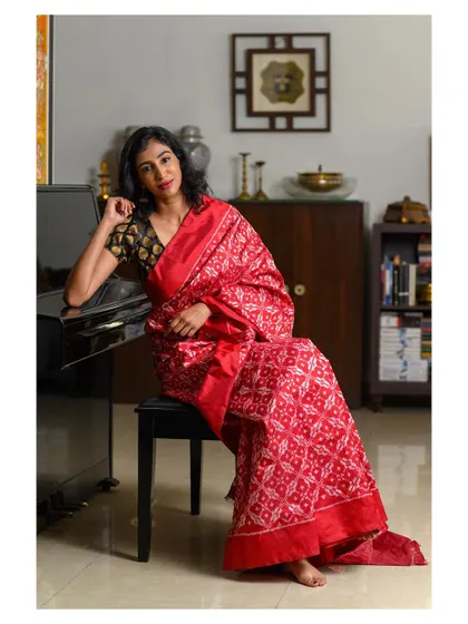 An elegant indoor portrait of a model in a red saree, seated at a piano. The setting adds a layer of classical sophistication.