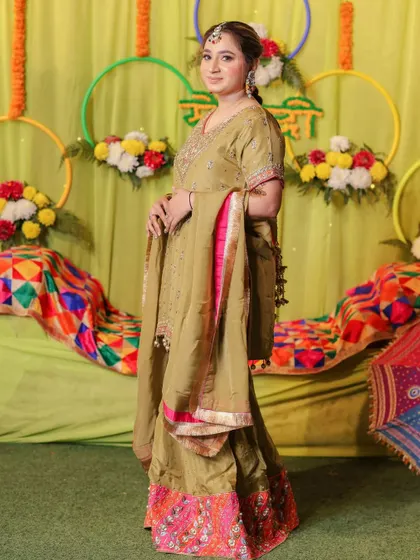A full-length shot of the bride at her Mehndi ceremony, showcasing her traditional outfit and the colorful decor.