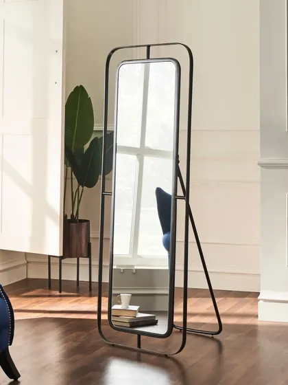 A full-length standing mirror with a modern black frame. The shot is composed to show the mirror's scale and design within a room, while the reflection adds a layer of interest.