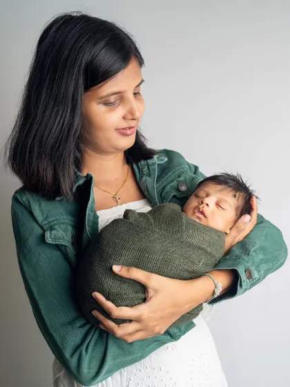 A mother cradling her sleeping baby, swaddled snugly in her arms. Our newborn sessions are calm and unhurried, allowing for these peaceful moments that show the deep love of a new mom.