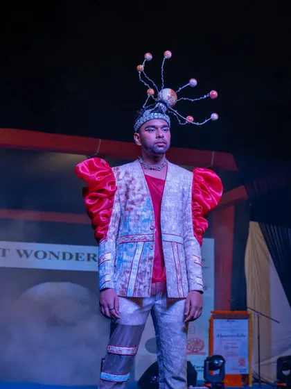 A male model presents a futuristic design with bold red puffed sleeves and a planetary headpiece.
