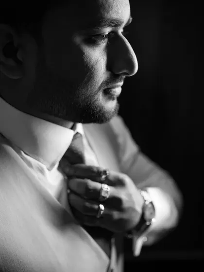 A dramatic black and white close-up of a groom adjusting his tie. This portrait is intense and cinematic, focusing on form and emotion.