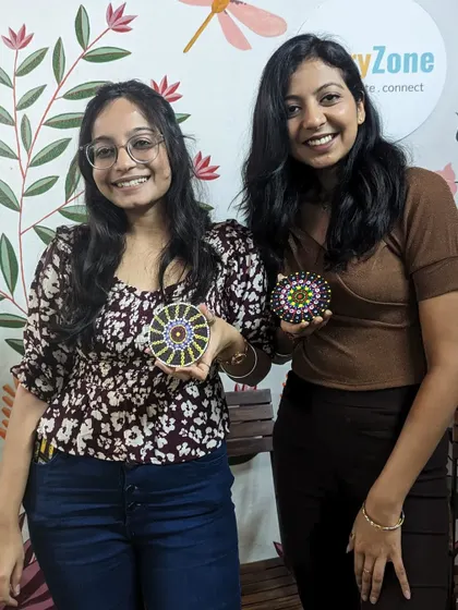 Two friends proudly showing off their mini dot mandala coasters. These small projects are a great introduction to the art form.
