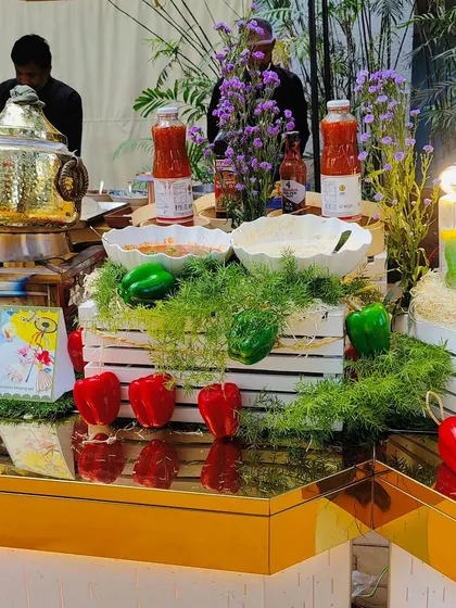 Our live station counter is decorated with fresh bell peppers, herbs, and flowers. This setup, featuring a golden serving dish, shows how we blend food and aesthetics to create an inviting atmosphere.