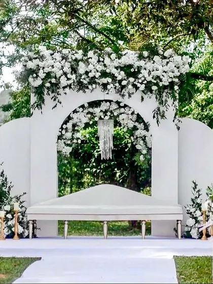 An all-white theme creates a timeless and elegant look. This outdoor stage features clean lines, modern white panels, and lush white floral arrangements, perfect for a sophisticated daytime ceremony.