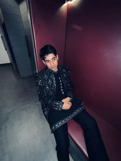 A candid shot of Ahsan Vazir seated, showcasing the detailed embroidery on the cuffs and hem of the black Indo-western kurta set.