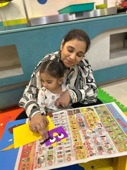 A mother helps her child decorate a craft with googly eyes, an activity that is always a hit with toddlers.