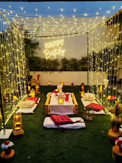 For a cozy and intimate celebration, I can create a beautiful cabana setup in your backyard. This design features a canopy of fairy lights, low picnic-style seating, and a neon sign for a personal touch.