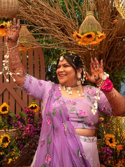 The bride, radiant in a purple lehenga, dances joyfully at her Haldi ceremony, surrounded by sunflower decor.