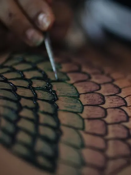 A macro shot showing the texture and detail of the colored henna paste as I fill in the mermaid scale pattern on the model's shoulder.