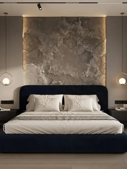 A textured stone accent wall provides a raw, organic element in this otherwise sleek and modern bedroom. The dark blue upholstered bed and simple globe pendant lights create a balanced and calming composition.