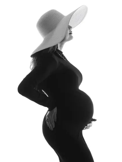 An elegant and artistic high-contrast silhouette. The mom-to-be wears a stylish hat, creating a chic and mysterious portrait that focuses entirely on her beautiful form.