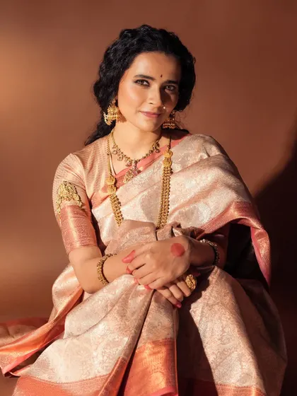 A full portrait from a fashion shoot featuring a beautiful silk saree. The makeup is warm and inviting, with softly curled hair and traditional gold jewellery completing the look.