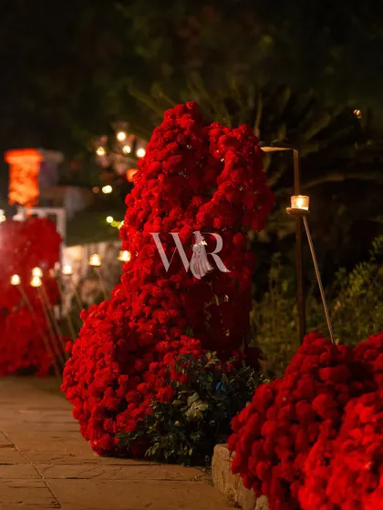 A close-up of one of the red floral sculptures lining the entrance path. The dense texture of the flowers creates a powerful statement of color and passion.