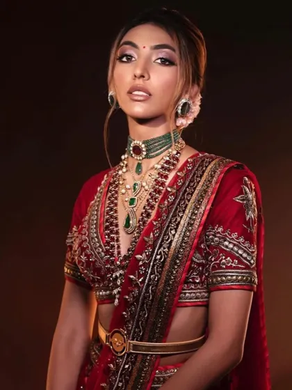 A traditional red bridal lehenga with a modern twist. The belted waist and layered jewelry are complemented by makeup that is both classic and contemporary.