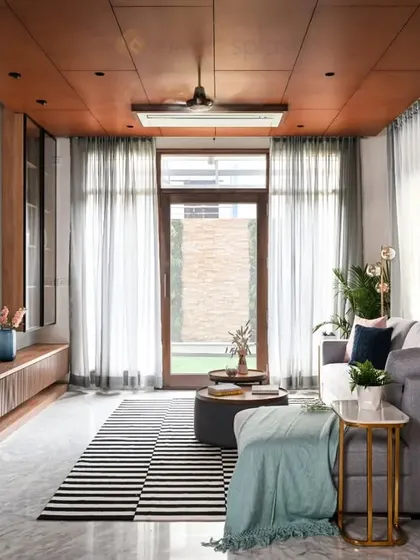 A contemporary living room with a wooden ceiling, a large grey sectional sofa, and a striped rug. The design feels spacious, modern, and connected to the outdoors.