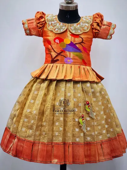 A unique pattu pavadai featuring a blouse with a hand-painted parrot motif. The mustard-colored skirt has matching parrot tassels, tying the whole theme together.