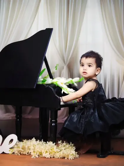 An elegant first birthday shoot with a baby girl in a black dress at the piano.