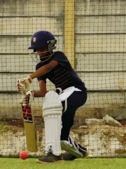 Eyes on the ball. A young cricketer, fully equipped with pads and helmet, is captured mid-shot during a practice session in the nets, demonstrating proper form and concentration.