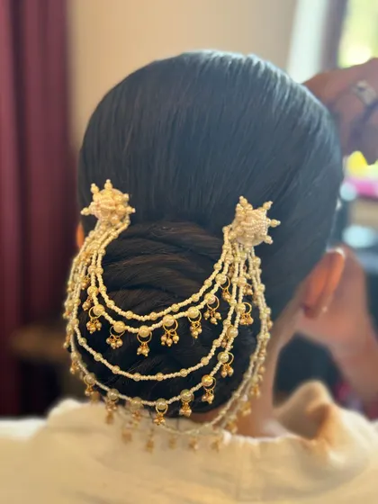 A classic bridal bun adorned with a multi-layered pearl hair accessory, known as a jhoomar. This adds a touch of royalty and is a beautiful alternative to flowers.