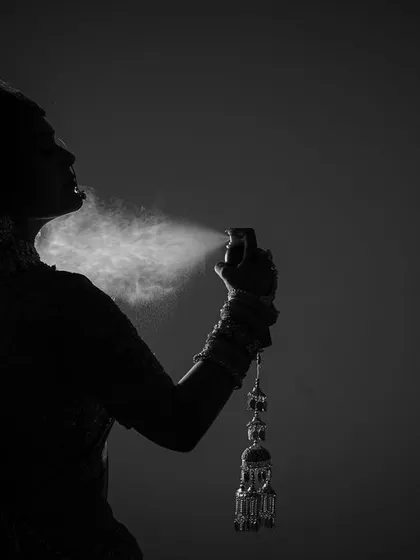 A creative black and white silhouette of the bride getting ready. This artistic shot captures the final touches, like a spray of perfume, in a unique and memorable way.