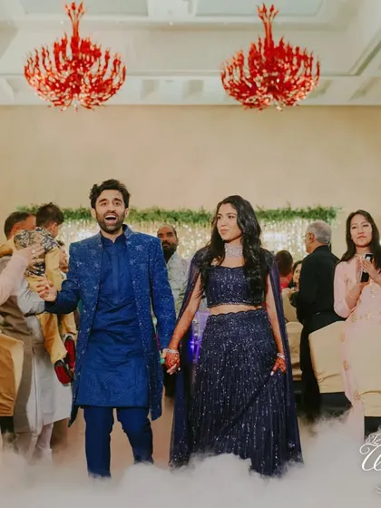 The couple making a grand Sangeet entrance through a cloud of low fog, hand-in-hand, ready to kick off the party.