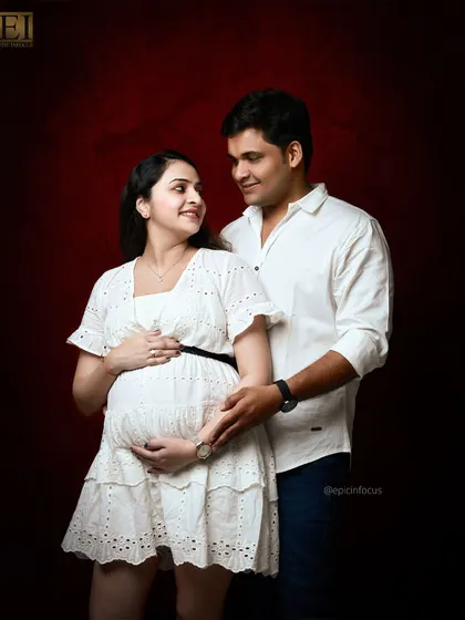 A classic studio portrait against a rich, red backdrop. The couple's white outfits create a striking contrast.