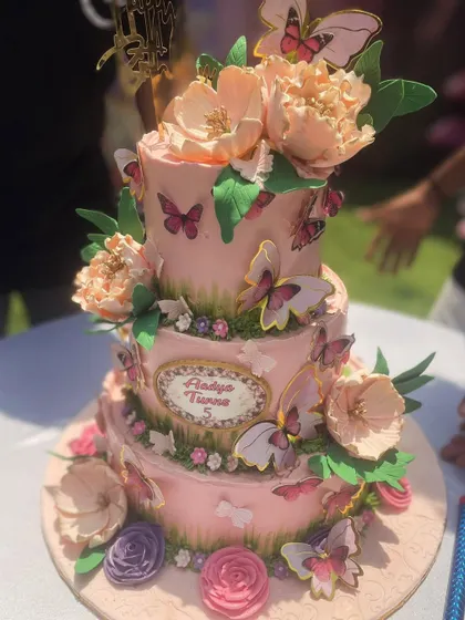 This beautiful three-tier butterfly cake was designed for a sunny outdoor celebration. It's adorned with delicate sugar flowers and dozens of fluttering butterflies, creating a truly enchanting garden party vibe.