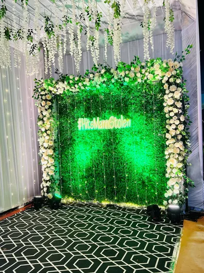 The green wall photo booth, with its bright neon sign, creates a striking contrast and a perfect backdrop for evening photos.