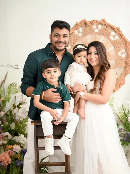 A lovely family portrait showcasing the bond between siblings. The older brother sits proudly next to his baby sister, held by their loving parents.