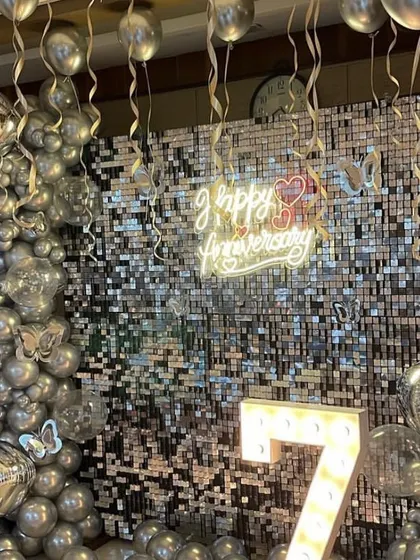 A glamorous 7th-anniversary celebration with a silver sequin shimmer wall. I framed it with a silver chrome balloon arch, added butterfly details, and hung more balloons from the ceiling to create a sparkling, festive atmosphere.