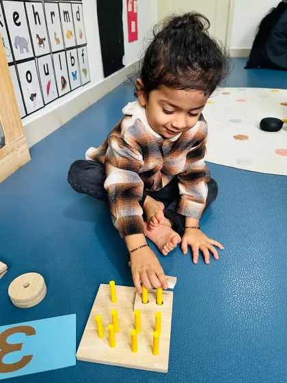 With a look of focus, this child practices counting with a wooden pegboard, reinforcing number recognition and one-to-one correspondence.