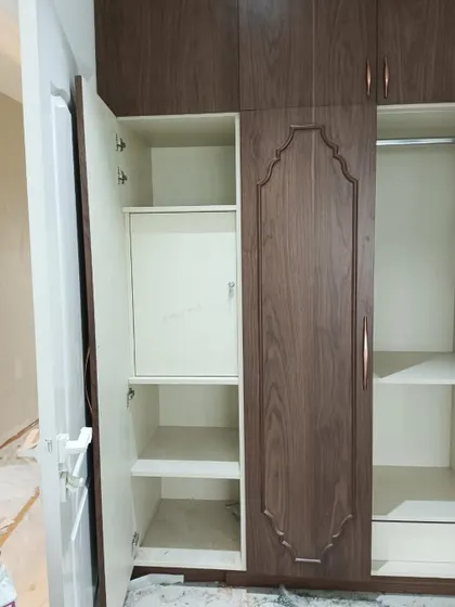 Custom wardrobes being installed on-site. This design features traditional carved details on the doors, adding a touch of heritage to the functional storage solution.