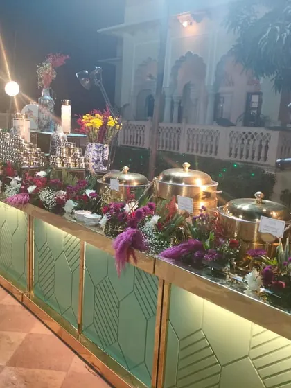 A lavish buffet display for a destination wedding at the Laxmi Vilas Palace. The setup is adorned with rich, colourful flowers and traditional brass serving dishes, reflecting the regal setting of the event.
