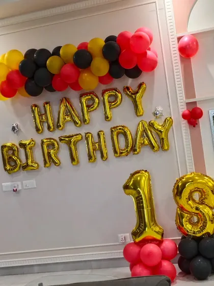 Celebrating an 18th birthday with a bold color scheme. This wall decoration uses red, yellow, and black balloons with large gold foil letters and numbers to mark the special occasion.