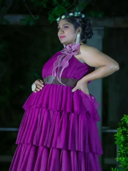 An elegant solo maternity portrait of a woman in a purple ruffled gown, posing gracefully in a garden at night.