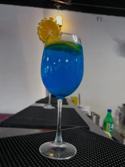 A bright blue curaçao mocktail garnished with an orange wheel. Shot at the bar, this image captures the fun and colorful side of a restaurant's drink menu.