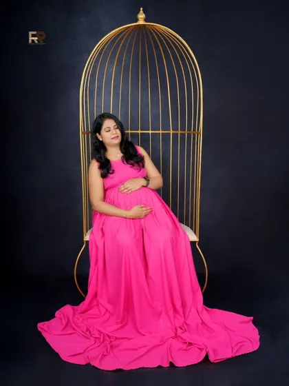 A bold and beautiful statement. The mom-to-be looks powerful and serene in a simple pink gown, seated in our golden birdcage prop against a solid black background.