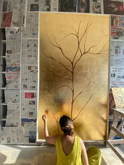 Painting the lower branches of the gold leaf tree. Working on a large-scale piece like this often means painting from all angles, including sitting on the floor.