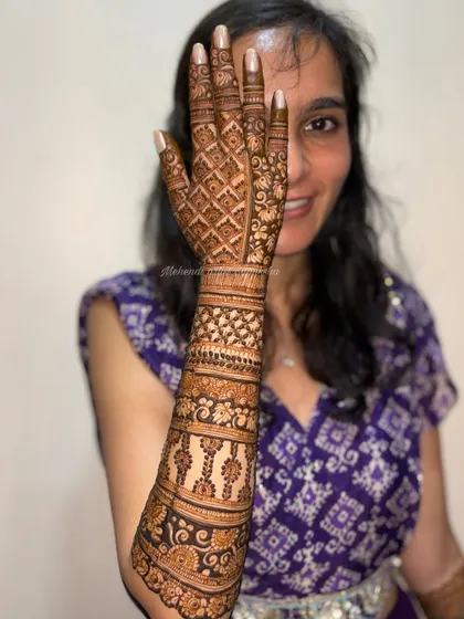 A smiling bride showing off her beautiful back-of-hand mehendi. The design is a perfect blend of traditional patterns and modern elegance.