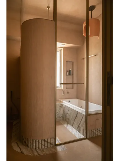 The bathtub is nestled in its own private alcove, with a large window providing natural light. The space feels earthy, curvy, and calm.