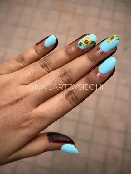 A cheerful and bright set of press-on nails with a sky blue base and two accent nails featuring hand-painted sunflowers.