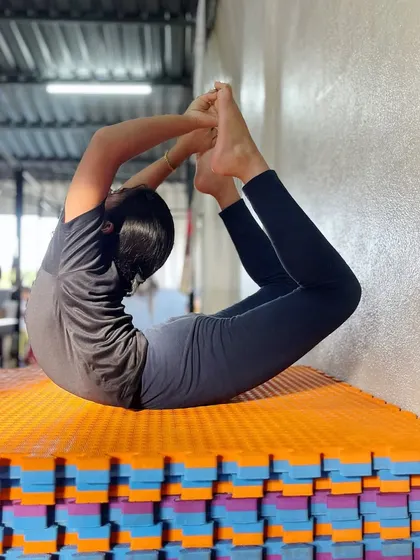 Discipline is the bridge between goals and accomplishments. This student uses the wall to assist with her bow pose, a smart way to safely deepen her backbend.