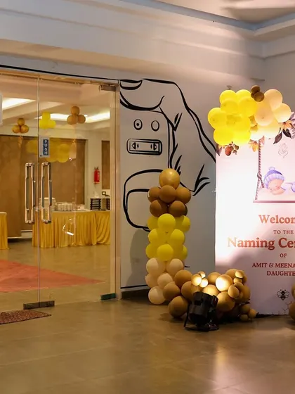 A welcoming entrance for a naming ceremony. This setup features a balloon arch in shades of yellow, brown, and peach over a personalized welcome sign, setting a warm and inviting tone for guests as they arrive.
