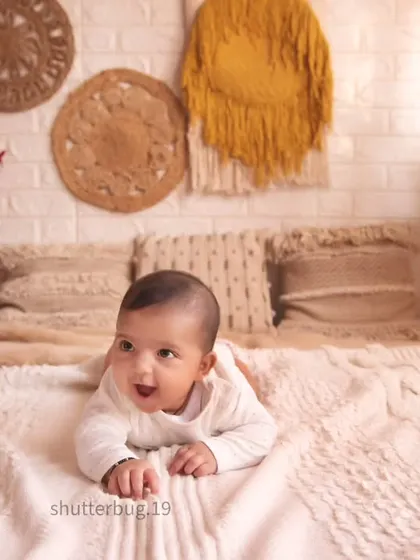 A wide shot of a happy baby during tummy time on a soft blanket. This photo is part of a larger family session that includes both individual shots of the baby and group portraits.