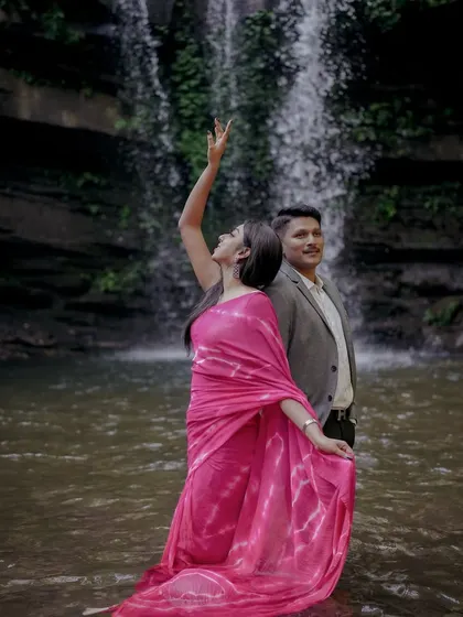 A couple poses by a waterfall, the bride's vibrant pink saree flowing into the water. This demonstrates our creative approach to incorporating natural elements into pre-wedding shoots.