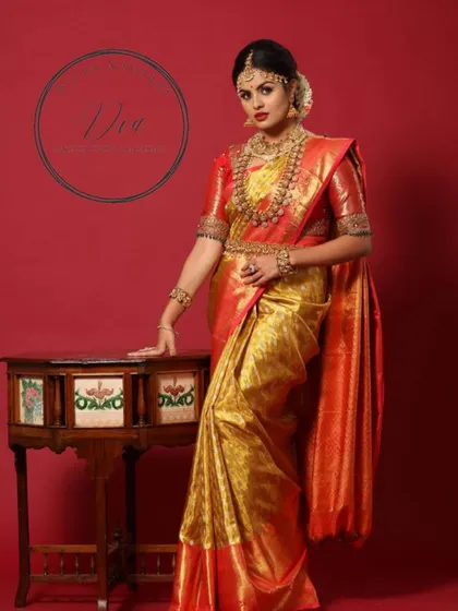 A full-length portrait of a model in a stunning red and gold Kanjeevaram saree. The makeup is classic bridal glam, with bold eyes and lips, paired with heavy temple jewellery for a majestic look.
