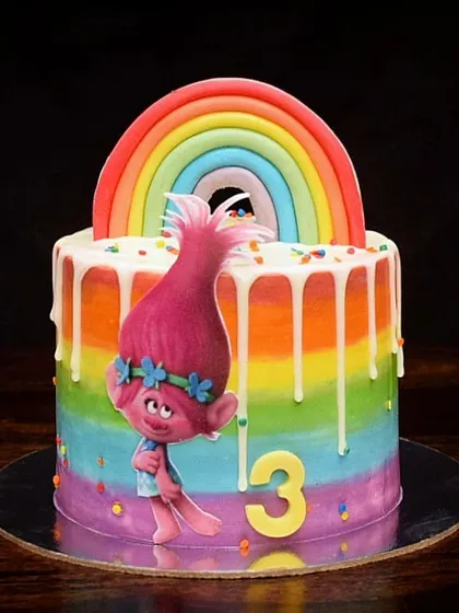 This colorful Trolls-themed cake is all about happiness and rainbows. It features a rainbow ombre buttercream exterior, a white chocolate drip, and a fondant rainbow topper, with Poppy front and center.